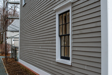 Corner view of a vintage tan coloured house with white trim and black wooden window spacers. The...