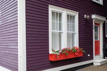 A purple painted exterior wall of a building with white trim. There's a double hung window, a...