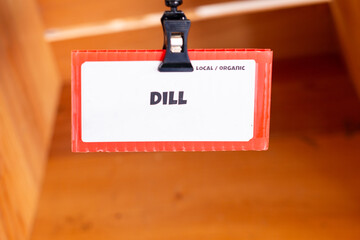 A white and vibrant red color cost sign for dill. The organic produce label has black text on white...