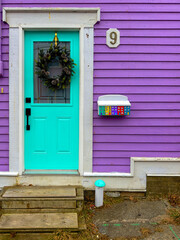 The exterior entrance to a country style house with purple wood clapboard siding, teal green glass...