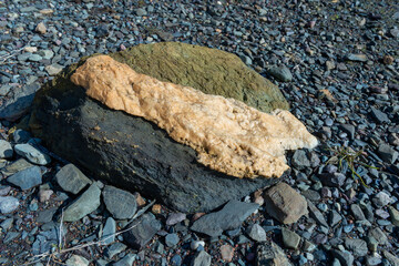 A three layered volcanic rock, green, white, and black color on a pebbled beach. The molten...