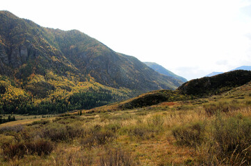 The hilly slopes of the mountain range form a picturesque valley in the early autumn evening in the rays of the setting sun.