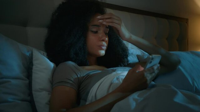 African American girl scrolling smartphone mobile phone online apps in bed before sleeping upset shocked ethnic woman customer worried internet problem loss connection error mistake bad news rejection