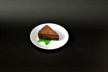 A plate with a piece of fresh chocolate cake decorated with mint leaves on a black background.