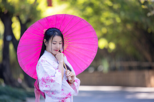 Asian woman wearing japanese traditional kimono. Beautiful Woman smiling, holding a umbrella walking outside. Woman in Kimono dress enjoying and walking on street outdoors in slow motion.
