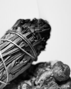 B & W Burning California White Sage and Sweetgrass Ceremonial Herb Bundle Resting on Rough Natural Green Prehnite Crystal Gemstone Mineral Against a White Backdrop