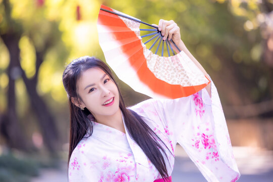 Asian woman wearing japanese traditional kimono standing on street.Beautiful Woman smiling ,holding hand fan to cover face. Woman in Kimono dress enjoying and walking on street outdoors in slow motion