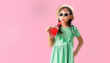 Happy Asian little girl posing with wear a hat and sunglasses holding glass of red sweet water,...