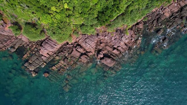 Aerial view of a lush coastline with rocky formations meeting the tranquil blue sea, depicting natural landscapes