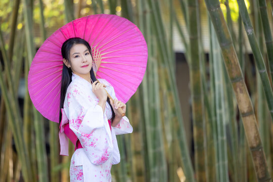 Asian woman wear Japanese kimono holding umbrella walking in the bamboo forest.Woman in Kimono dress enjoying,walking on street outdoors in slow motion.Beautiful Woman standing on street.