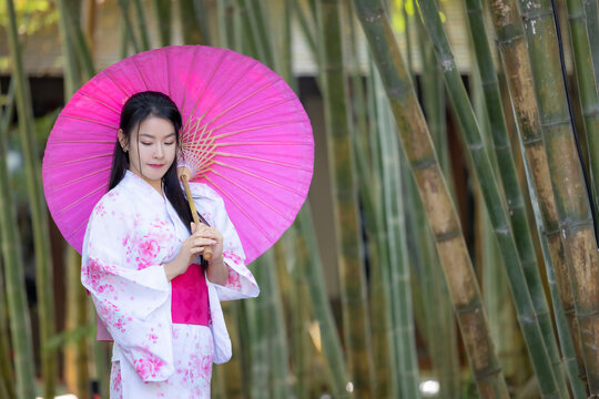 Asian woman wear Japanese kimono holding umbrella walking in the bamboo forest.Woman in Kimono dress enjoying,walking on street outdoors in slow motion.Beautiful Woman standing on street.