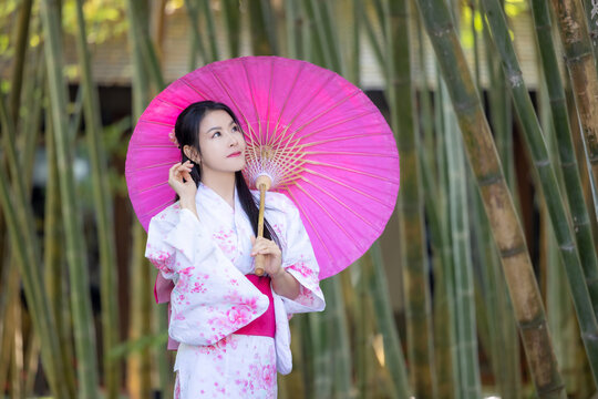 Asian woman wear Japanese kimono holding umbrella walking in the bamboo forest.Woman in Kimono dress enjoying,walking on street outdoors in slow motion.Beautiful Woman standing on street.