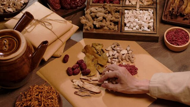 Close-up of a physician selecting each type of dry medicinal herb to put into a medicine package, next to a medicinal kettle on a wooden table. Traditional Chinese medicine.