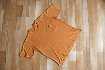 Flat lay mockup brown t-shirt with pocket on wooden floor