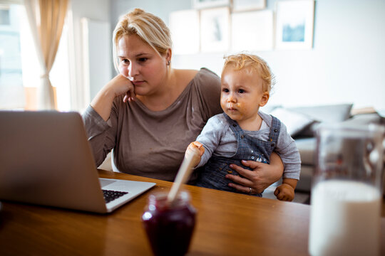 Young worried single mother using a laptop with her baby toddler son in her lap