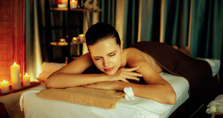 Obraz na płótnie Canvas Caucasian woman customer enjoying relaxing anti-stress spa massage and pampering with beauty skin recreation leisure in warm candle lighting ambient salon spa at luxury resort or hotel. Quiescent
