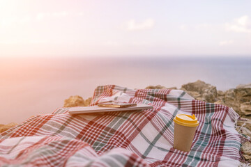 Obraz premium Laptop coffee on blanket with ocean view. Illustrating serene outdoor laptop use. Freelancer enjoying their time outdoors while working or browsing the internet.