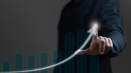 Business growth concept. Businessman uses index finger with glowing arrow tip on graph showing business growth on dark background. - obrazy, fototapety, plakaty