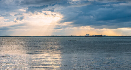 a small boat crossing the bay while there is a cargo ship anchoring nearby.