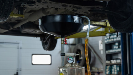 The process of changing the oil in a car engine. Draining old dark used oil from a car on a lift. 