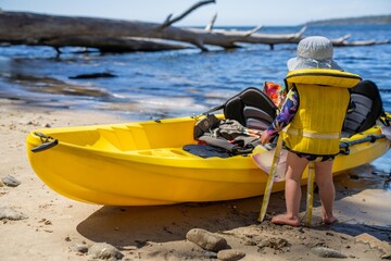 toddler wearing a lifejacket in a kayak on a sandy beach on holiday in summer in australia