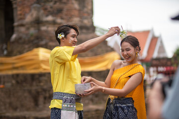 A beautiful Young Thai couple wearing Thai costumes playing in the water during Songkran in the...