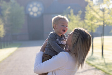 This delightful capture features a young Caucasian woman lifting a toddler into the air, both...