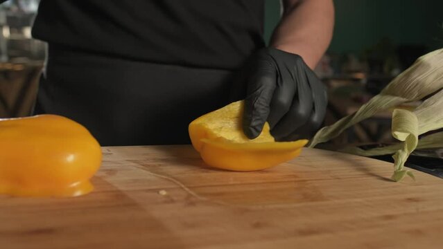 Chef cutting yellow bell pepper on cutting board with kitchen knife