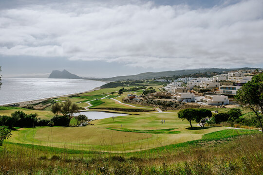 Sotogrande, Spain - January, 23, 2024 - A golf course overlooking the sea with the Rock of Gibraltar in the distance and residential buildings to the side.