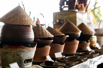 A lineup of traditional clay pot rice warmers, topped with iconic bamboo hats, evoking the warmth and authenticity of Asian culinary heritage and craftsmanship in Northern Thai restaurant