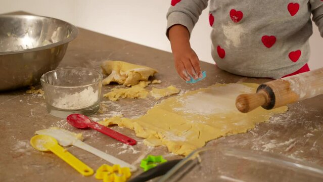 manos de niña latina morena vestida de rojo amasando harina de trigo preparado para hornear galletas o pan casero con utensilios de cocina rodillo