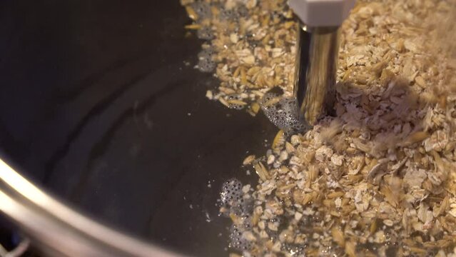 Crushed malt is added to hot water in a stainless steel brew kettle for start of mashing process - close up view of beer making