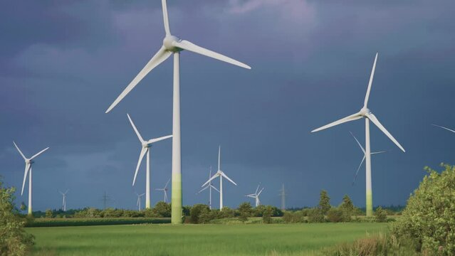 Rotating wind turbines in the green field. Dark stormy sky in the background.