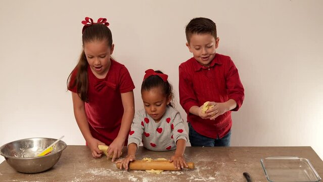 Niños felices hermanos vestido de rojo con corazones sobre la mesa mezclando mantequilla y con el rodillo preparando masa para hornear galletas deliciosas leche mantequilla