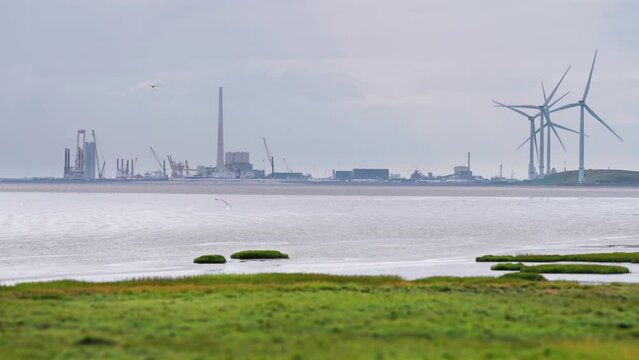 A city wrapped in haze and rotating wind turbines on the Danish coast.