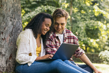 Multiracial couple studying in the park with laptop