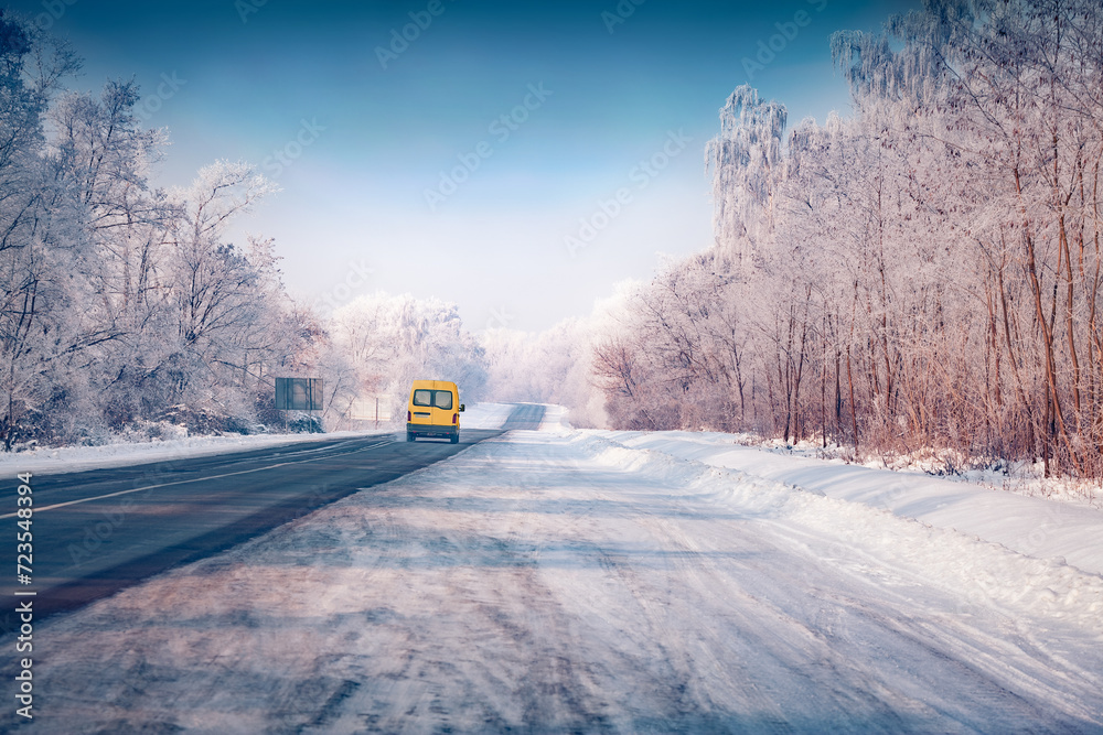 Poster Yellow van on the asphalt road. Splendid winter view of frosty trees on both sides of the road. Cold morning scene of distant way. Traveling concept background. Beautiful winter scenery.