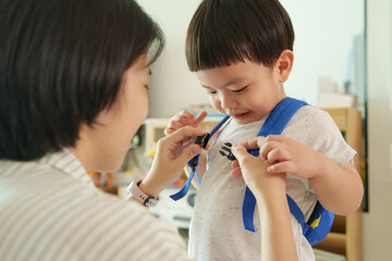 Mother help son to fasten buckle on backpack strap