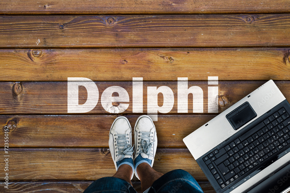 Poster Legs in sneakers standing next to laptop and Delphi on wooden floor. Delphi programming language.

