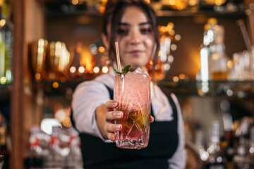Young bartender offering a drink at the bar of a cocktail bar