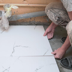 A male builder tiler lays floor ceramic tiles. Selective soft focus