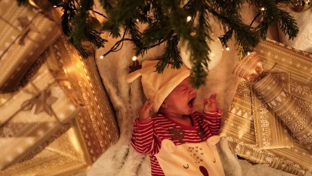 Cute newborn baby boy crying under the Christmas tree wearing adorable reindeer clothes.