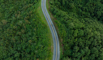 Aerial view of dark green forest road and white electric car Natural landscape and elevated roads Adventure travel and transportation and environmental protection concept	