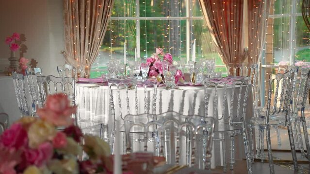Shot of fancy wedding reception tables with glasses and plates, table is decorated with gorgeous pink and white roses and white candles, panning shot