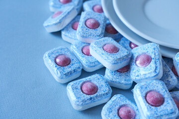 White plates and dishwasher tablets on blue background. Selective focus. Close-up.