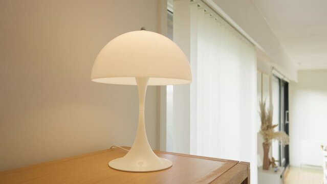 Minimalist white table lamp on a wooden desk in a bright room.