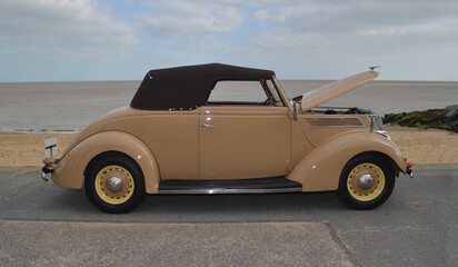Vintage Ford Club Cabriolet parked on seafront promenade beach ad sea in background.