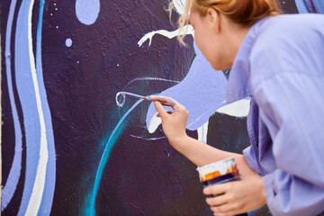 Female painter draws picture with paintbrush on canvas for outdoor street exhibition, close up back side view of female artist apply brushstrokes to canvas infusing life into outdoor art space