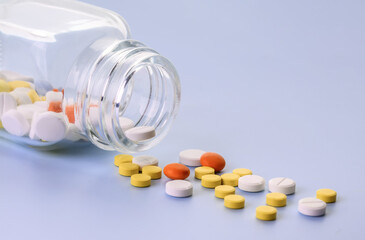 Multicolored Pills spilling out from transparent glass medicine bottle. Copy space