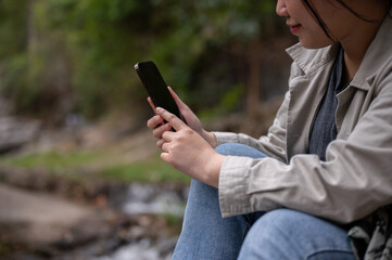 A cropped shot of an Asian woman using her phone while taking a break during her hiking trip.